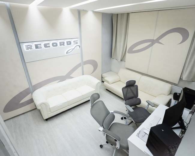 The image shows a modern office space with a white sofa, a gray office chair, a desk with a computer, and "RECORDS" displayed on the wall.