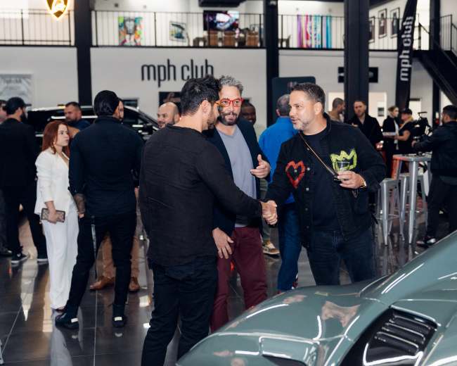 A group of people socialize in a luxury car showroom, accompanied by high-end vehicles on display.