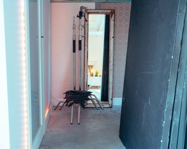 The image shows a narrow corridor with a mirror and a stack of black chairs supported by a tripod stand positioned at the end.