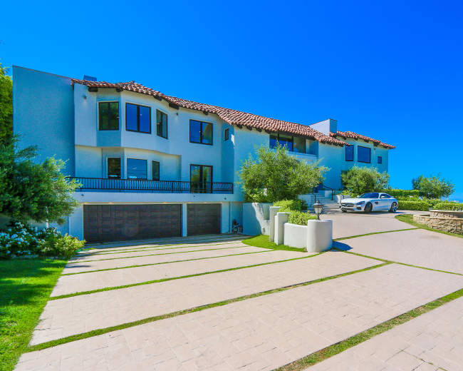 A modern two-story house with a tile roof, large windows, and a spacious driveway leads up to it.