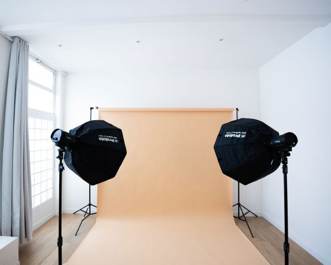 A photography studio with two softbox lights positioned in front of a plain orange backdrop.