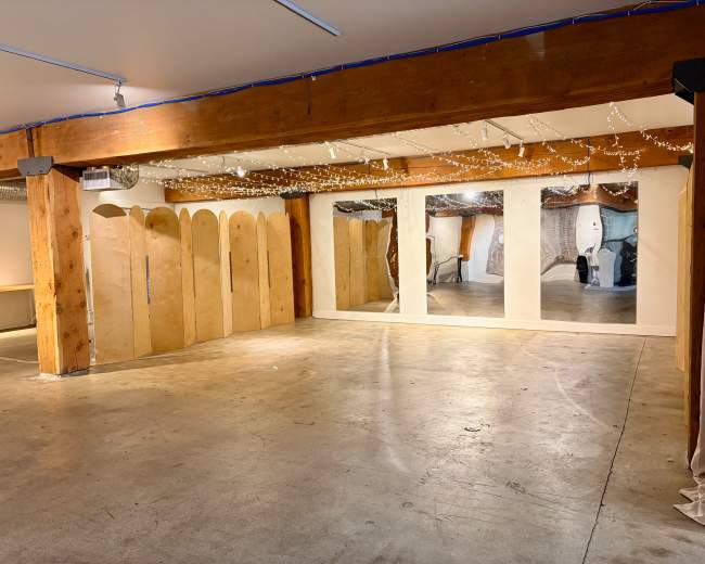 The image shows an empty room with wooden beams, decorative lights, and mirrored panels against the walls.