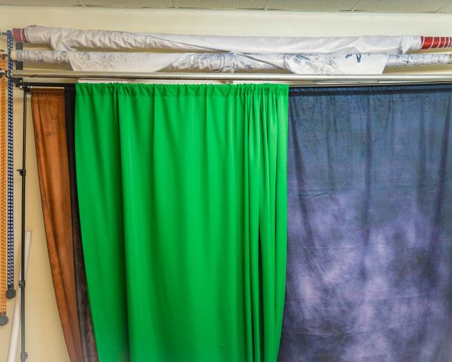 A set of fabric curtains in various colors hanging from a rack against a wall.