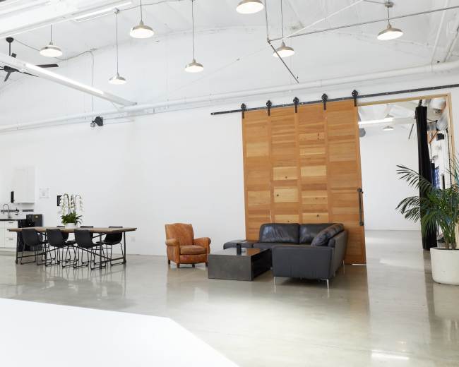 The image shows a spacious, modern open-plan interior featuring a kitchen area, a dining table, and a seating arrangement with a large wooden sliding door.