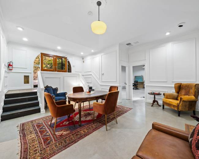 A well-lit entryway with a seating area that includes a round table and four chairs, flanked by a set of stairs leading to another level.