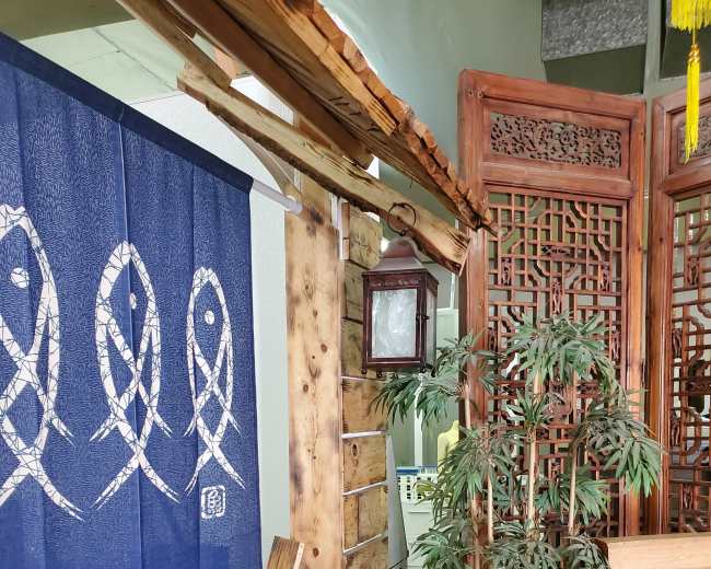 A wooden entrance featuring a blue fabric curtain with fish designs, flanked by decorative wooden screens and a potted plant.