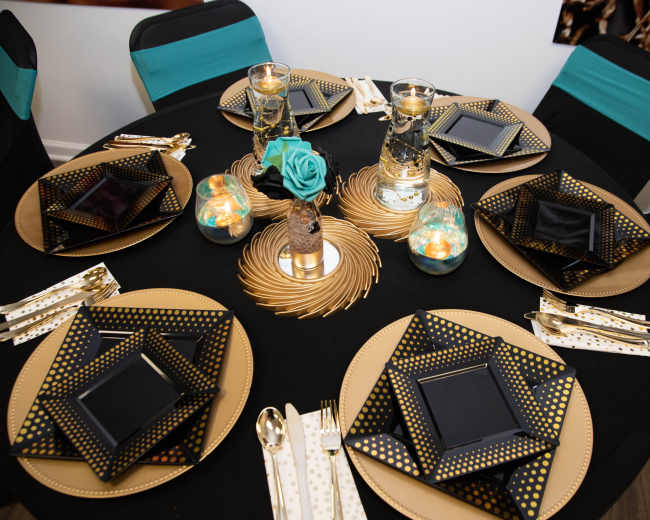 An elegantly set dining table with black and gold plates, decorative candles, and turquoise accents.
