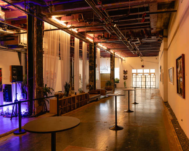 The image shows a spacious interior corridor featuring tables, artwork on the walls, and a glass door leading outside.