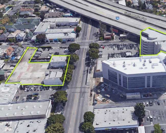 The image shows aerial view of a construction site featuring multiple commercial buildings and parking areas alongside a freeway.