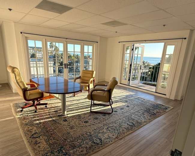 A conference room features a round table surrounded by four chairs and large windows that provide a view of the outdoors.