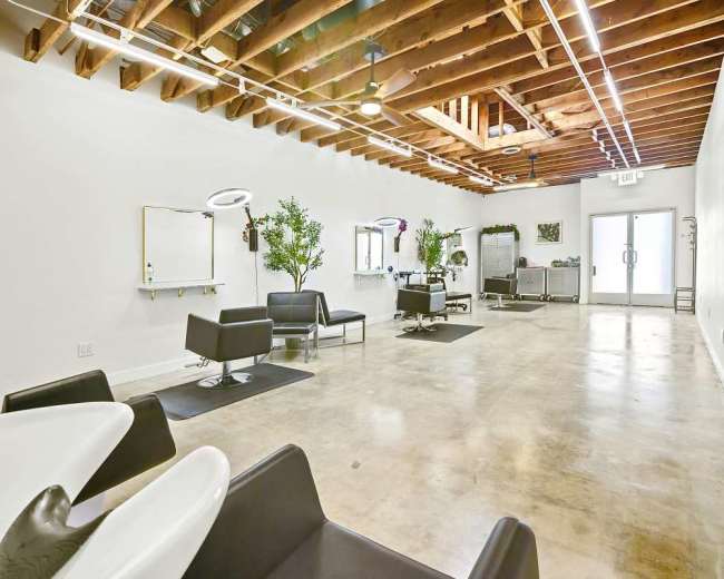 A spacious, well-lit interior of a hair salon features black seating, hair washing stations, and greenery against white walls.