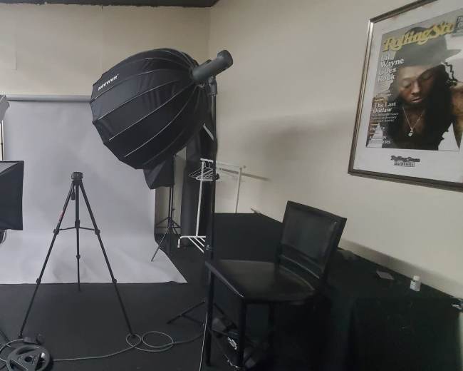 The image shows a photography studio featuring lighting equipment, a backdrop, a tripod, and a seating area.