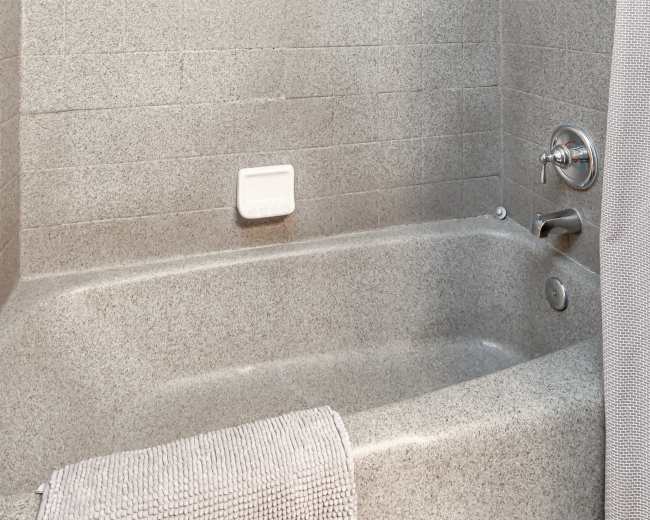 The image shows a tiled bathroom featuring a shower and a bathtub with a soap dish and a towel hanging on the side.