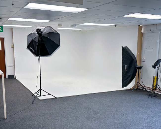 A photography studio with a white backdrop, two softbox lights on tripods, and a gray carpeted floor.