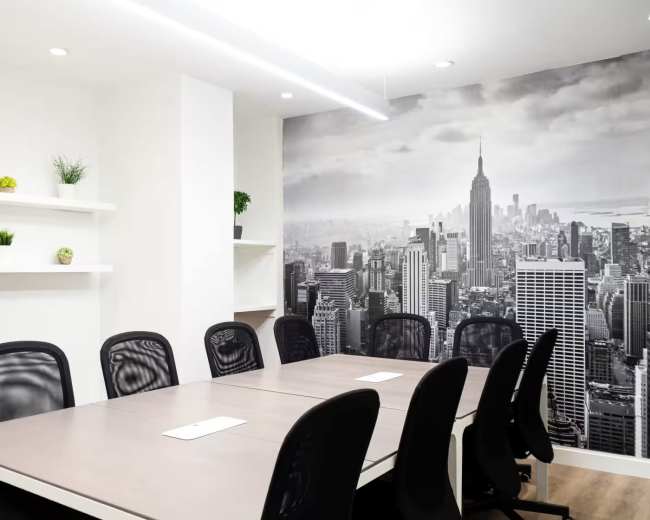 A modern conference room features a large table surrounded by black chairs and a backdrop of a cityscape mural.