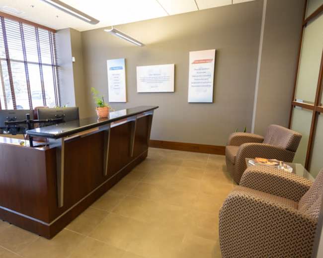 The image shows a modern reception area with a front desk, two chairs, and informational wall displays.