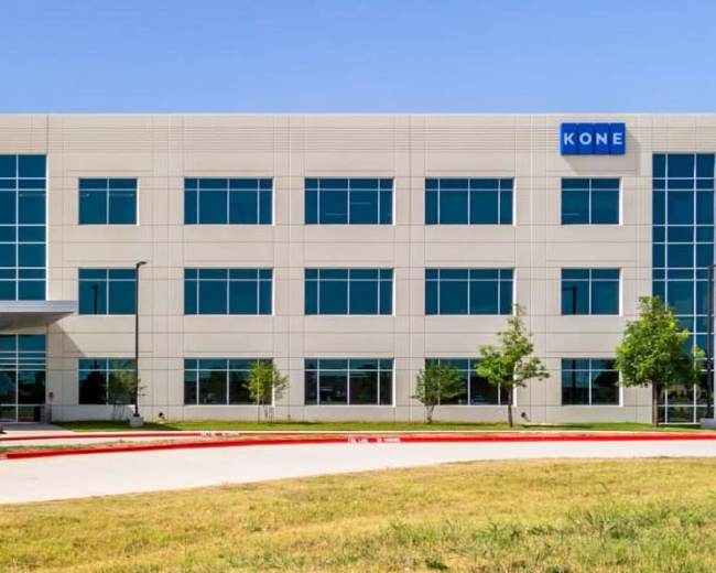 The image shows a modern office building with large glass windows and a prominent sign displaying "KONE."