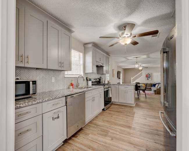 A modern kitchen features gray cabinets, stainless steel appliances, and a light-colored backsplash, with a dining area visible in the background.
