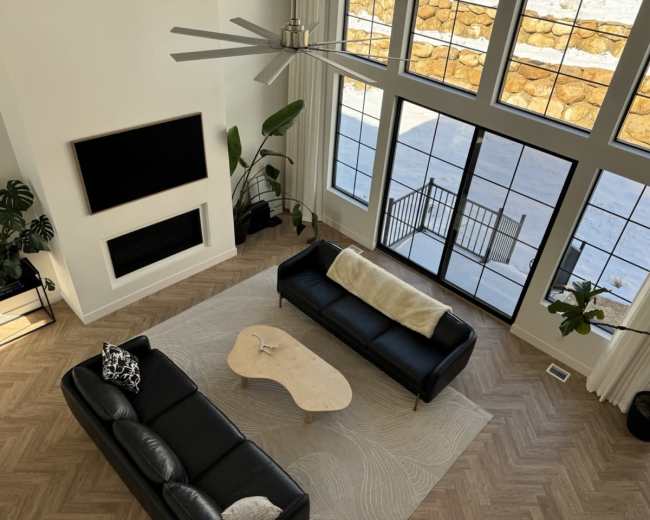 A spacious living room features two black sofas facing a large window with a view of a snowy landscape.