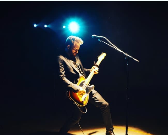 A guitarist performs on stage under a spotlight.