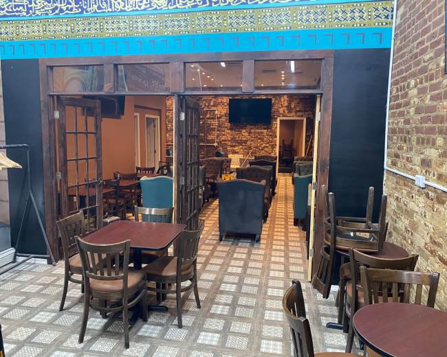 The image shows an indoor dining area of a restaurant featuring wooden furniture and a tiled floor, with an open entrance leading to another room.