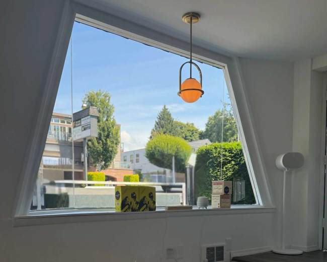 A colorful rug with various toys is placed on a wooden floor in front of a large window featuring a triangular design and a view of greenery outside.