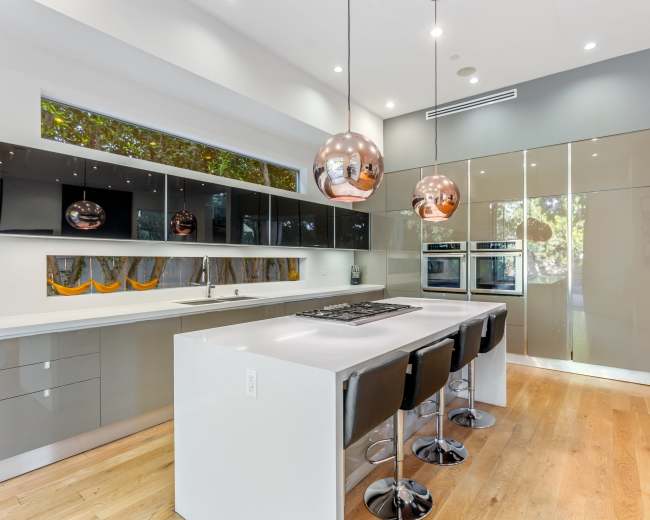 The image shows a modern kitchen with sleek cabinetry, a central island with four bar stools, and pendant lights hanging above.