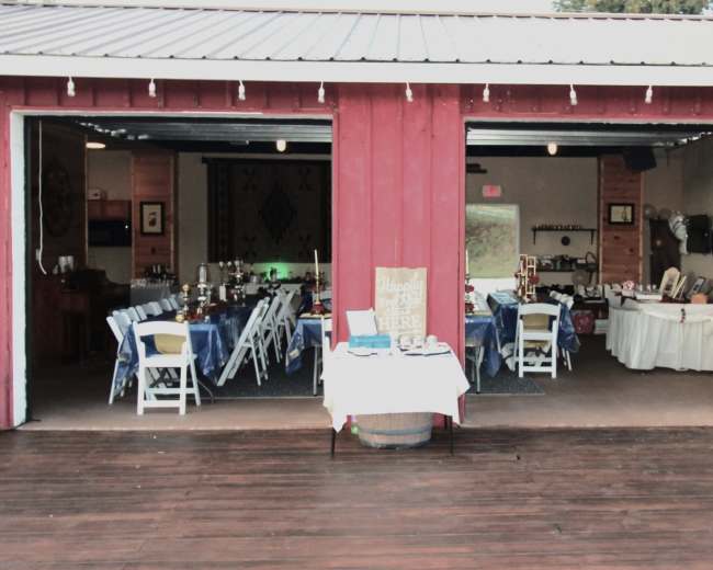 The image shows a rustic venue with two open sections filled with dining tables, decor, and festive lighting.