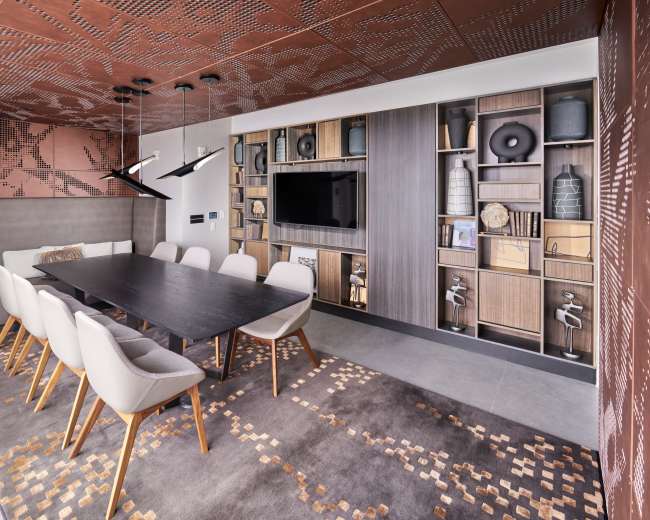 A modern conference room features a long black table surrounded by white chairs, with a backdrop of stylish wall décor and a built-in media unit.
