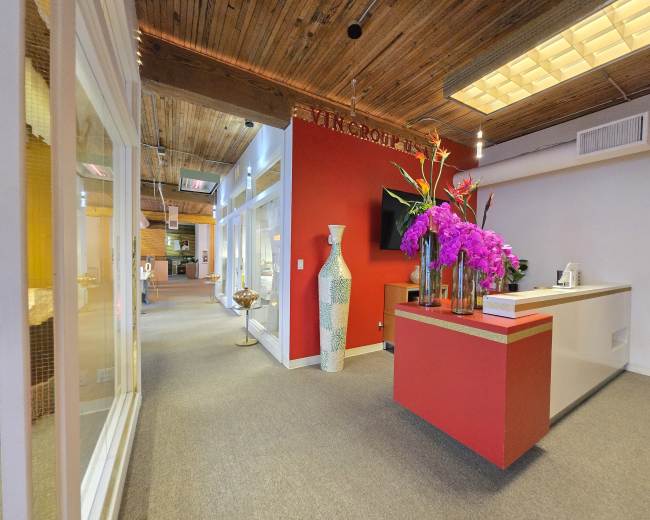 The image depicts a modern office reception area with a red accent wall, white reception desk, and decorative flowers.