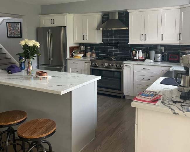 A modern kitchen with white cabinets, a marble-topped island, and stainless steel appliances.