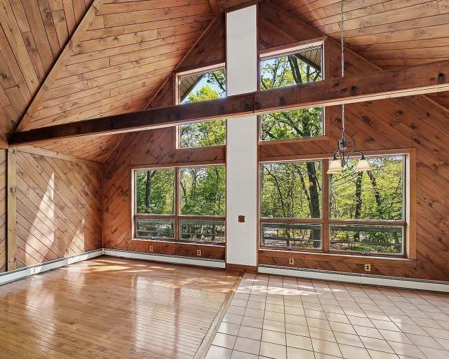 The interior features a vaulted wooden ceiling with large windows overlooking a forested area.