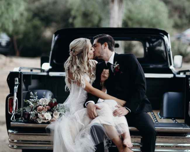 A bride and groom share a kiss while sitting on the tailgate of a pickup truck decorated with flowers.