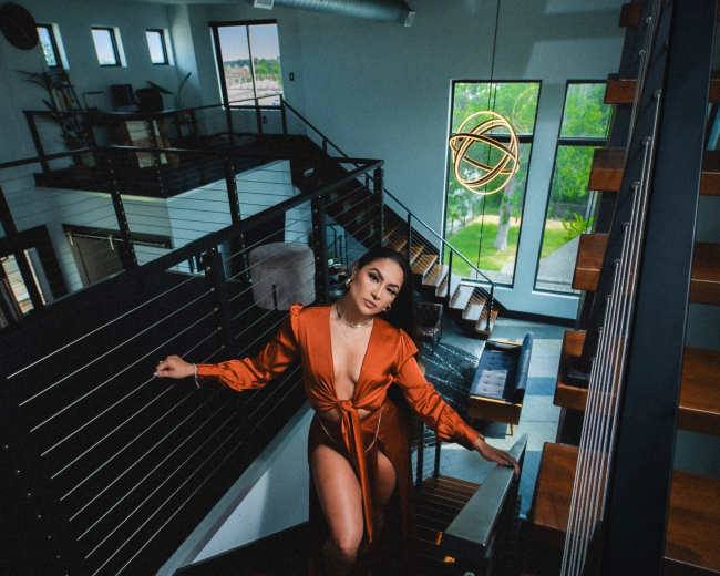 A woman in an orange dress poses on a staircase in a modern, well-lit building with large windows.