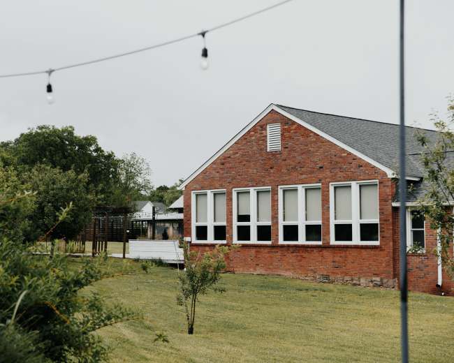 A brick house with multiple windows is surrounded by a green lawn and trees.