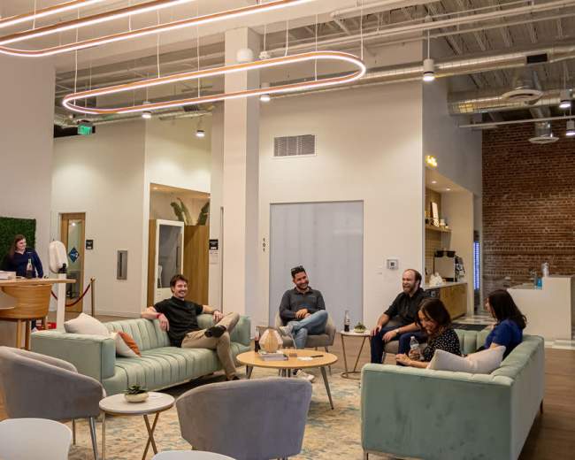 A group of five people relaxes in a modern lounge area with light-colored couches and a tall moss wall in a well-lit space.