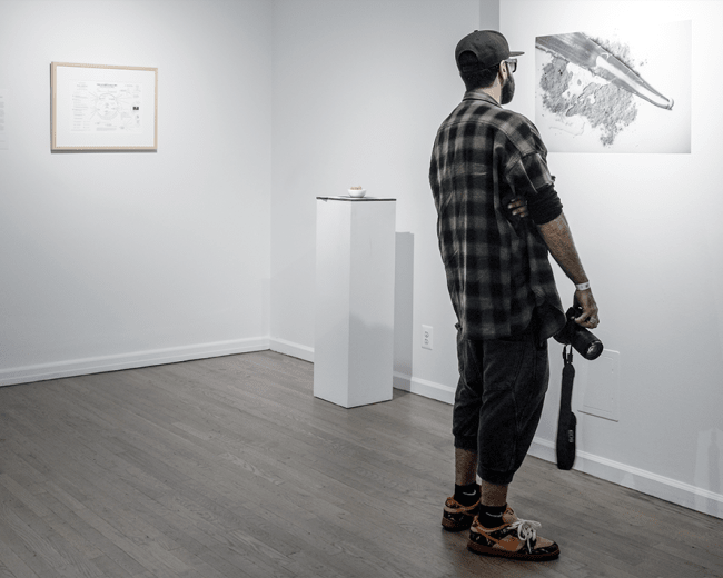 A man stands in an art gallery, observing a large black-and-white photograph of a whale displayed on the wall.