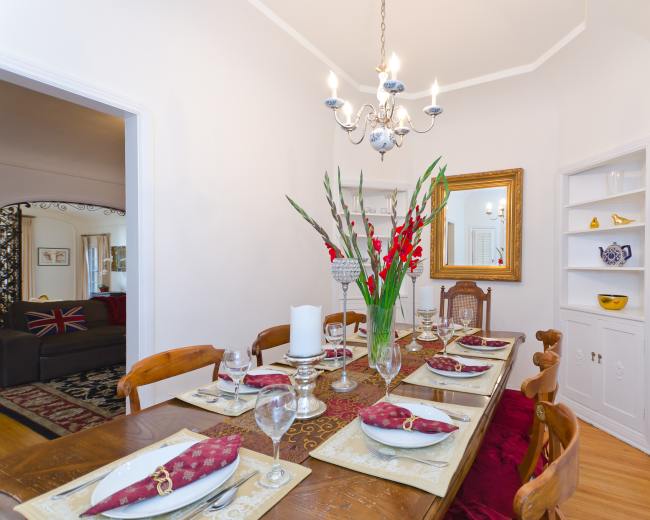 A dining table set with elegant place settings and a floral centerpiece, illuminated by a chandelier in a well-decorated dining room.