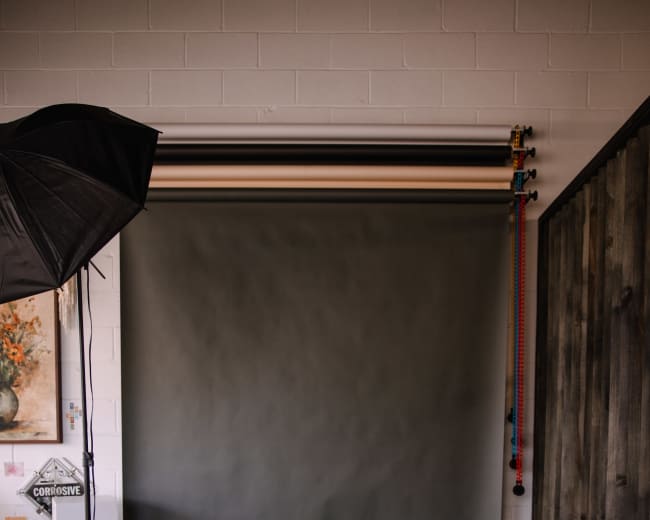 A photography studio setup featuring a gray backdrop, light stands, and softboxes positioned on a tiled floor.