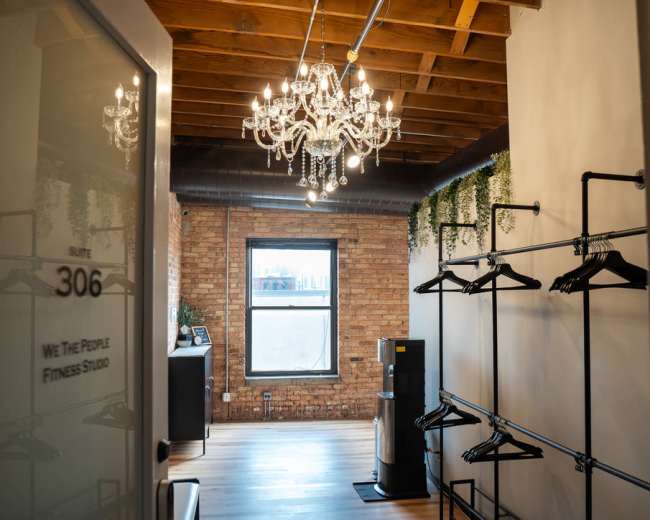 A bright room with wooden flooring features a chandelier, a window with a view, and racks for clothing along the walls.