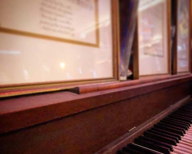 A close-up view of an old piano's keys with framed documents visible in the background.