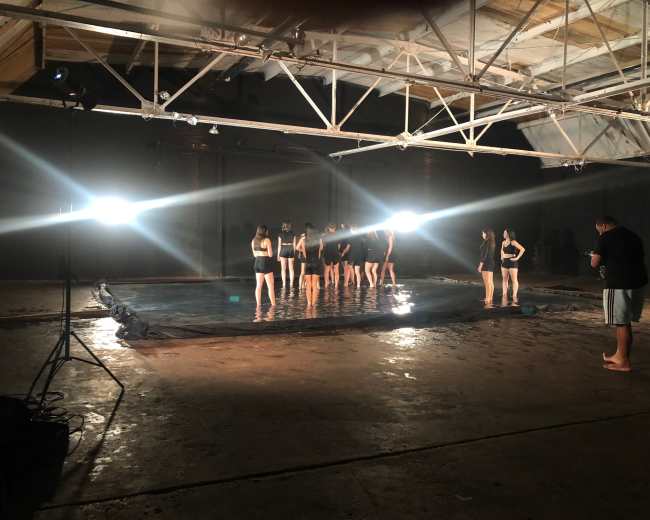 A group of individuals stands in a pool of water illuminated by bright lights in an industrial space.