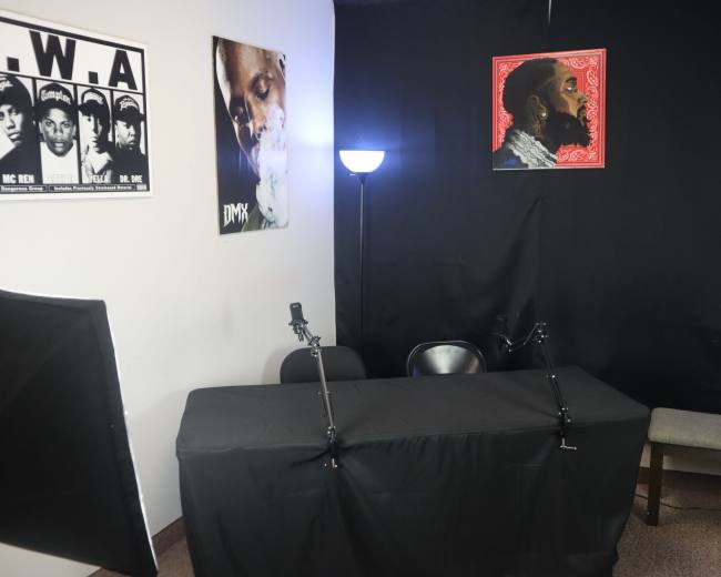 A small recording studio setup with a table covered in a black cloth, two microphones on stands, and posters of DMX and N.W.A on the walls.