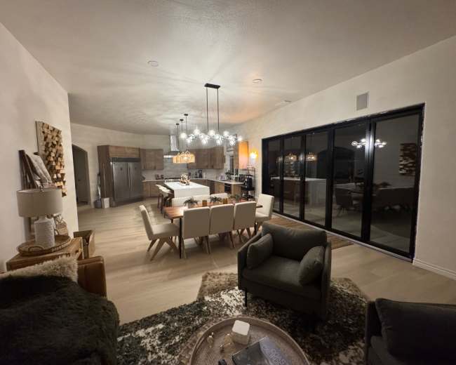 A modern living and dining area features a large table with chairs, a kitchen island, stylish lighting fixtures, and glass sliding doors that open to an outdoor space.
