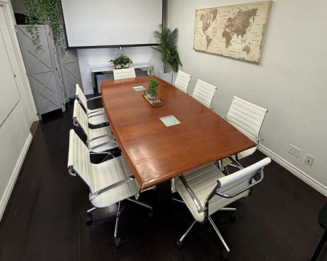 The image shows a conference room with a large wooden table surrounded by white leather chairs, a screen at the front, and a world map on the wall.