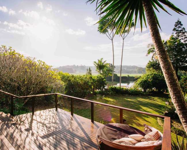 A wooden deck overlooks a lush green landscape with trees and a sunlit sky in the background.