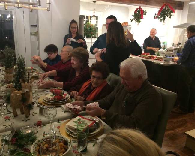A group of people gathers around a dining table adorned with festive decorations while sharing a meal during a holiday celebration.