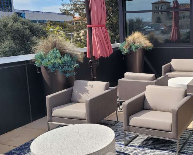 A modern outdoor terrace featuring gray seating arrangements, a round table, and tall potted plants.