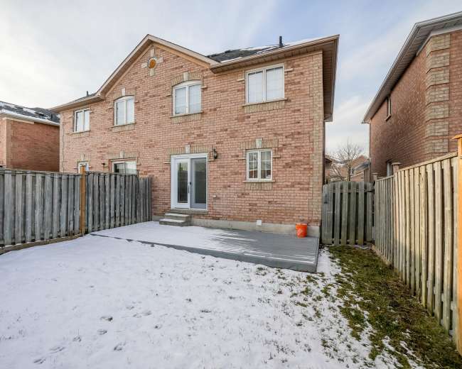 A two-story brick house with a partially snow-covered backyard and a wooden fence surrounding the property.