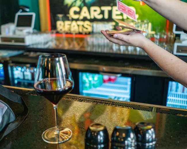 A person performs a card trick at a bar while a glass of red wine sits on the counter.